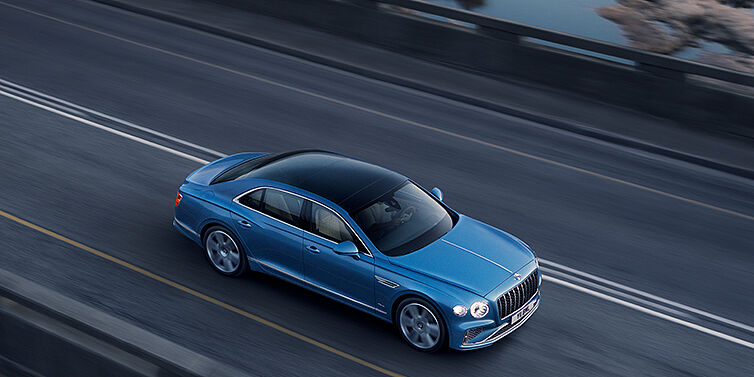 Bentley Tbilisi New Bentley Flying Spur Azure sedan in Light windsor blue paint by Mulliner, with 22 inch Azure wheels seen from overhead driving dynamically on a country road