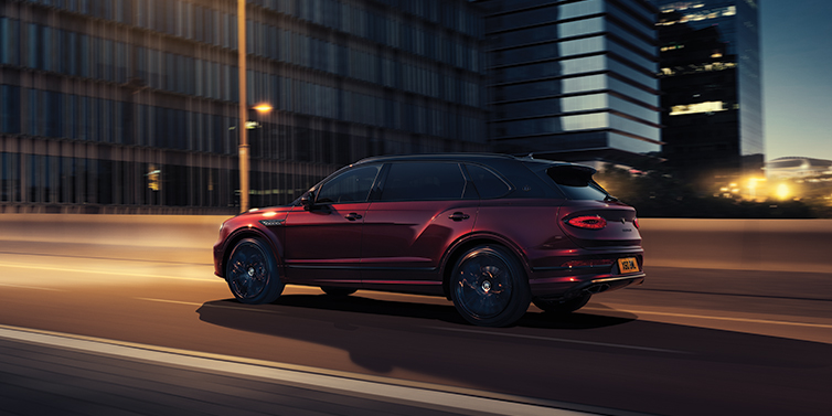 Bentley Tbilisi Bentley Bentayga Extended Wheelbase Mulliner SUV in Cricket Ball red paint driving dynamically in city at night